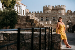 Hannah sitting in front of a gate in old town rhodes with the castle in the background