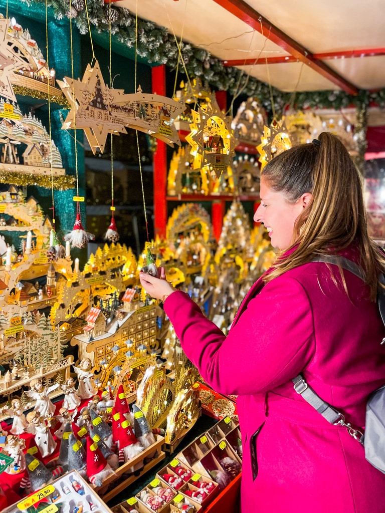 Hannah, wearing a berry-coloured coat, browsing a stall of wooden Christmas ornaments 
