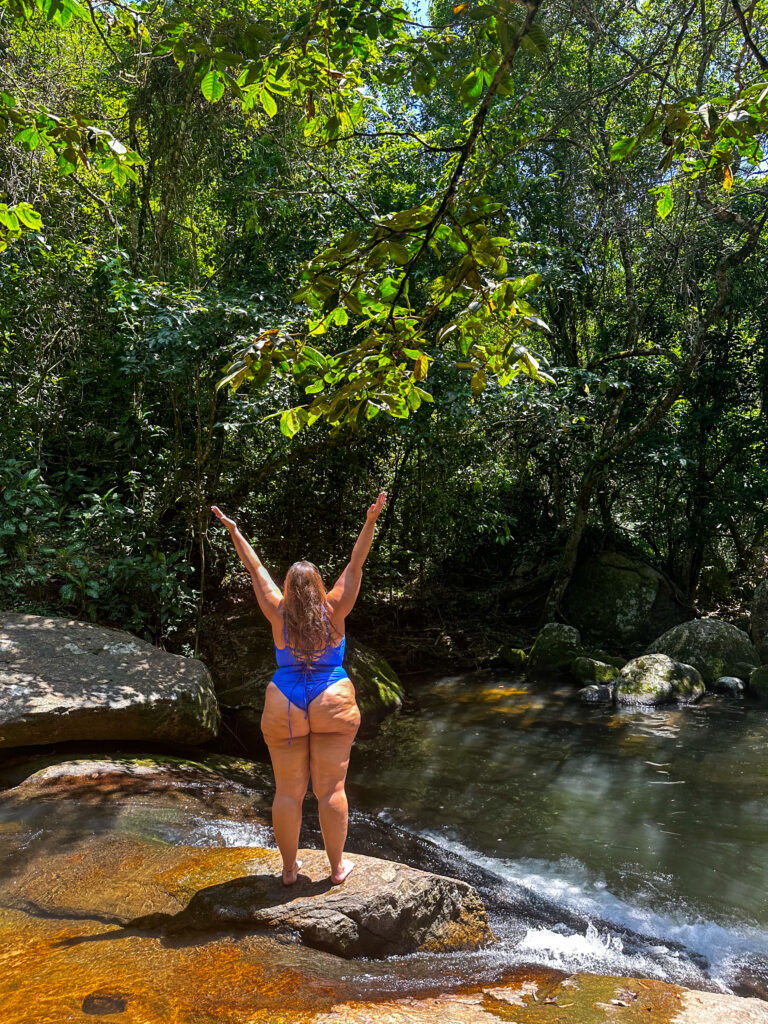 Hannah in a blue swimsuit with her arms in the air ready to slide down the waterfall