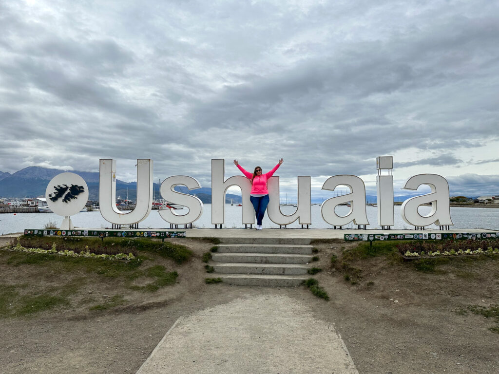 Hannah Logan with her arms in the air posing with the Ushuaia sign