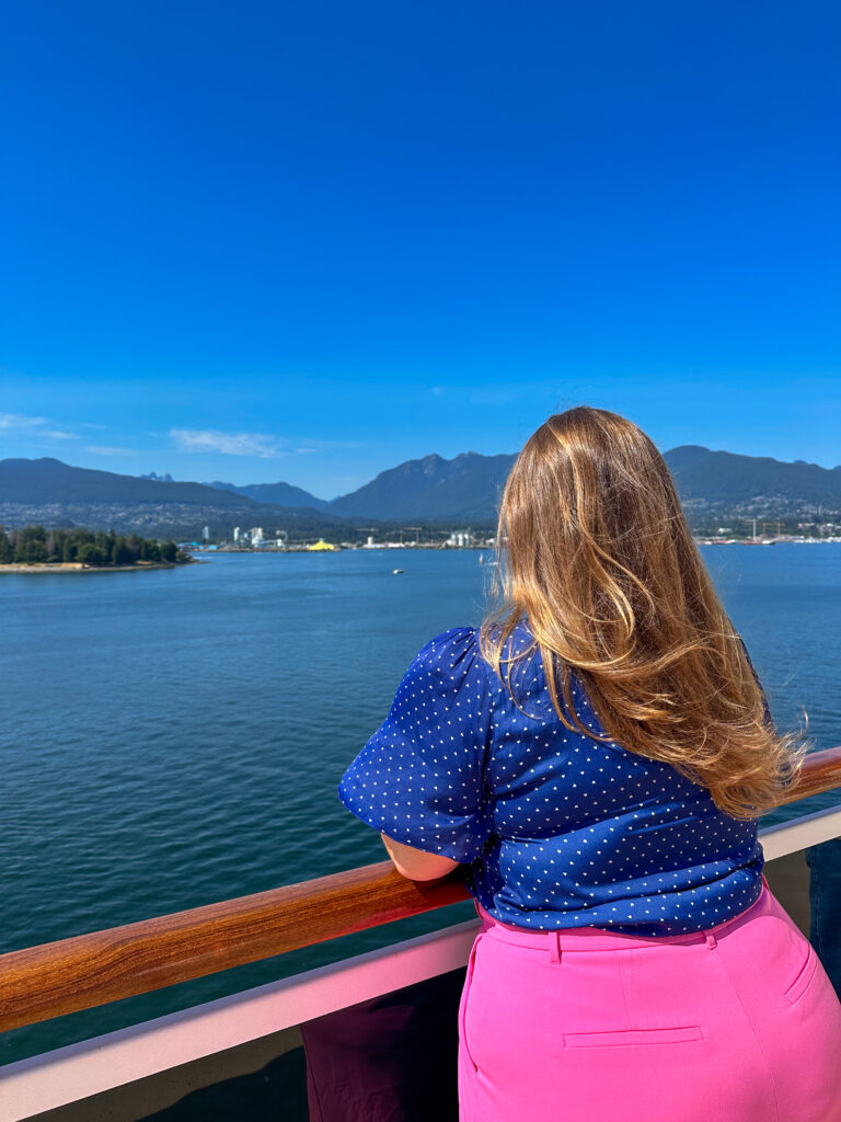 Hannah in pink pants and a blue shirt looking over the balcony of her ship at Vancouver