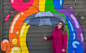 Hannah in front of a mural with a paint rainbow and umbrella