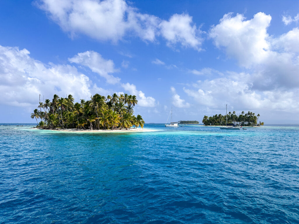 Two uninhabited islands with bright blue water and a blue sky with puffy white clouds