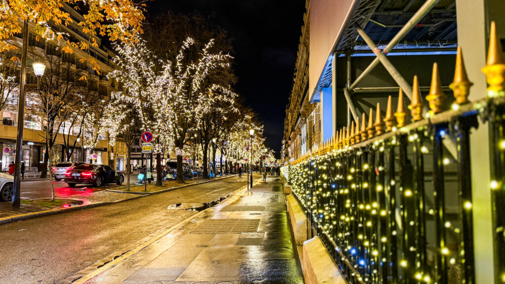 The streets of Paris lit up with white, twinkling lights on the trees, buildings, and railings